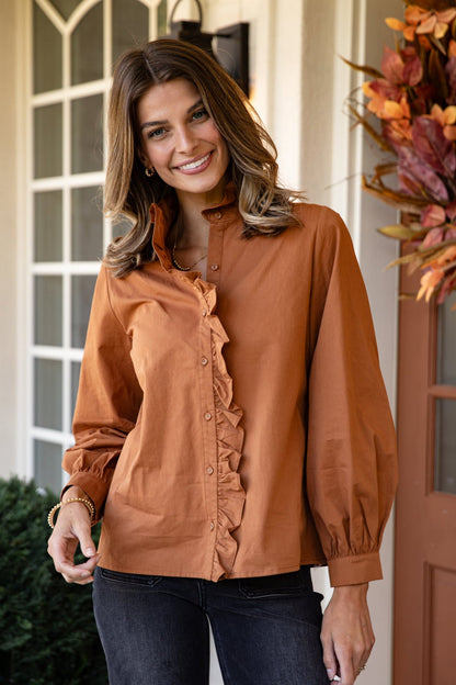 Woman wearing a brown blouse with ruffles standing in front of a door with autumn decorations.