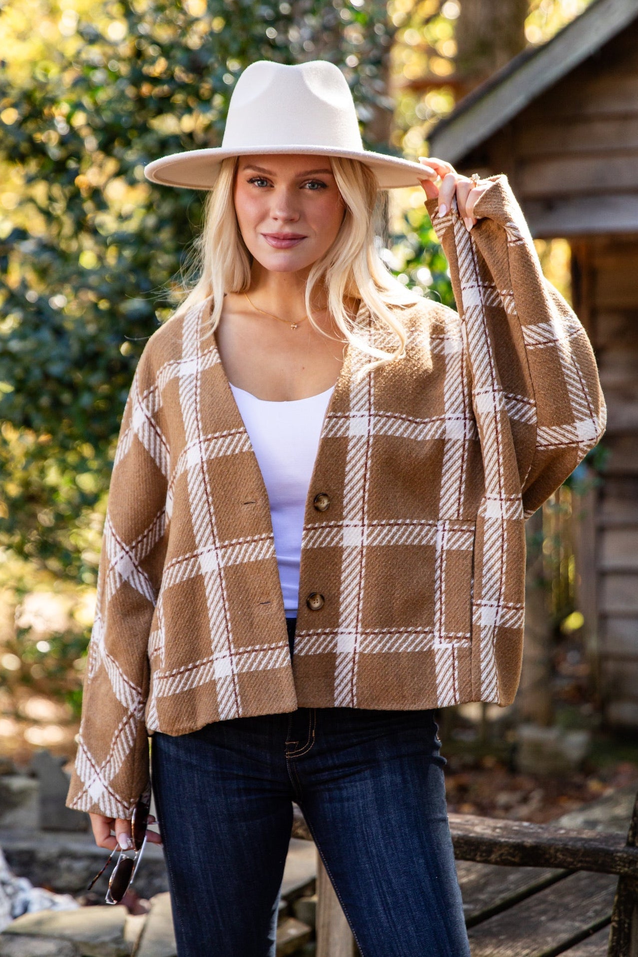 Woman wearing a plaid jacket and hat outdoors with a cabin in the background