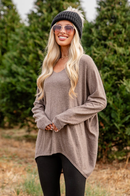Woman in a beige sweater and black leggings standing in front of trees
