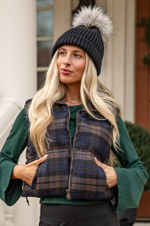 Woman wearing a plaid vest over a green jacket in front of a house with Christmas decorations.