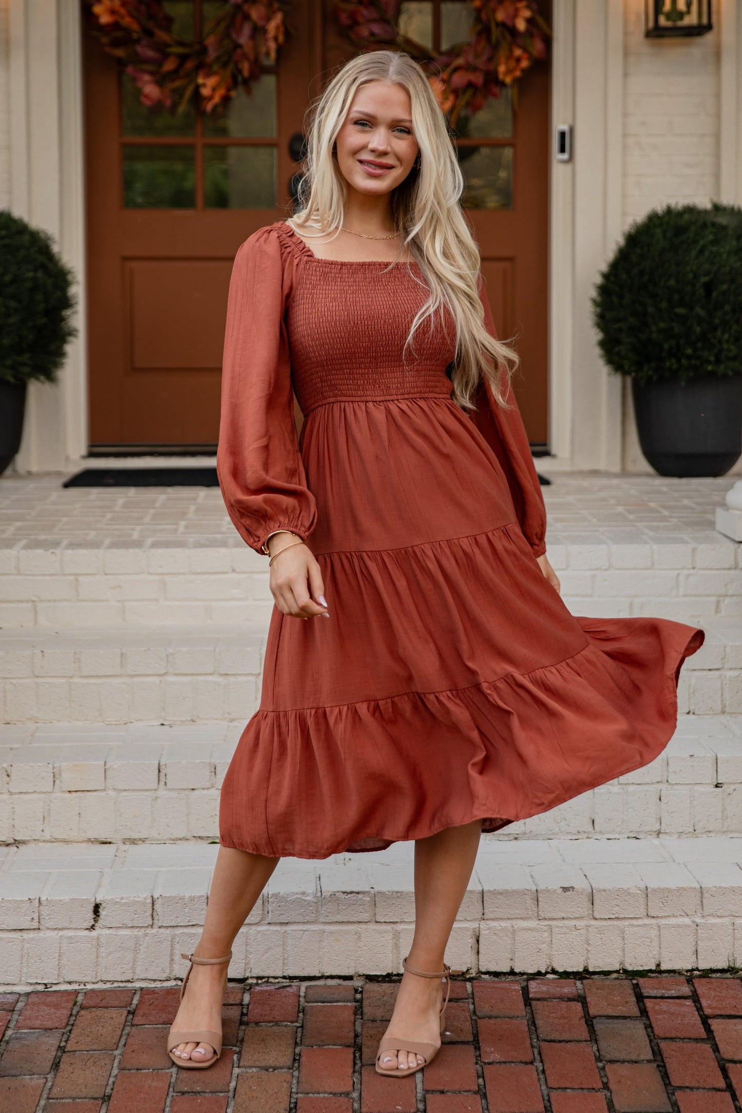 Woman in a rust-colored dress standing on a porch with autumn decorations.