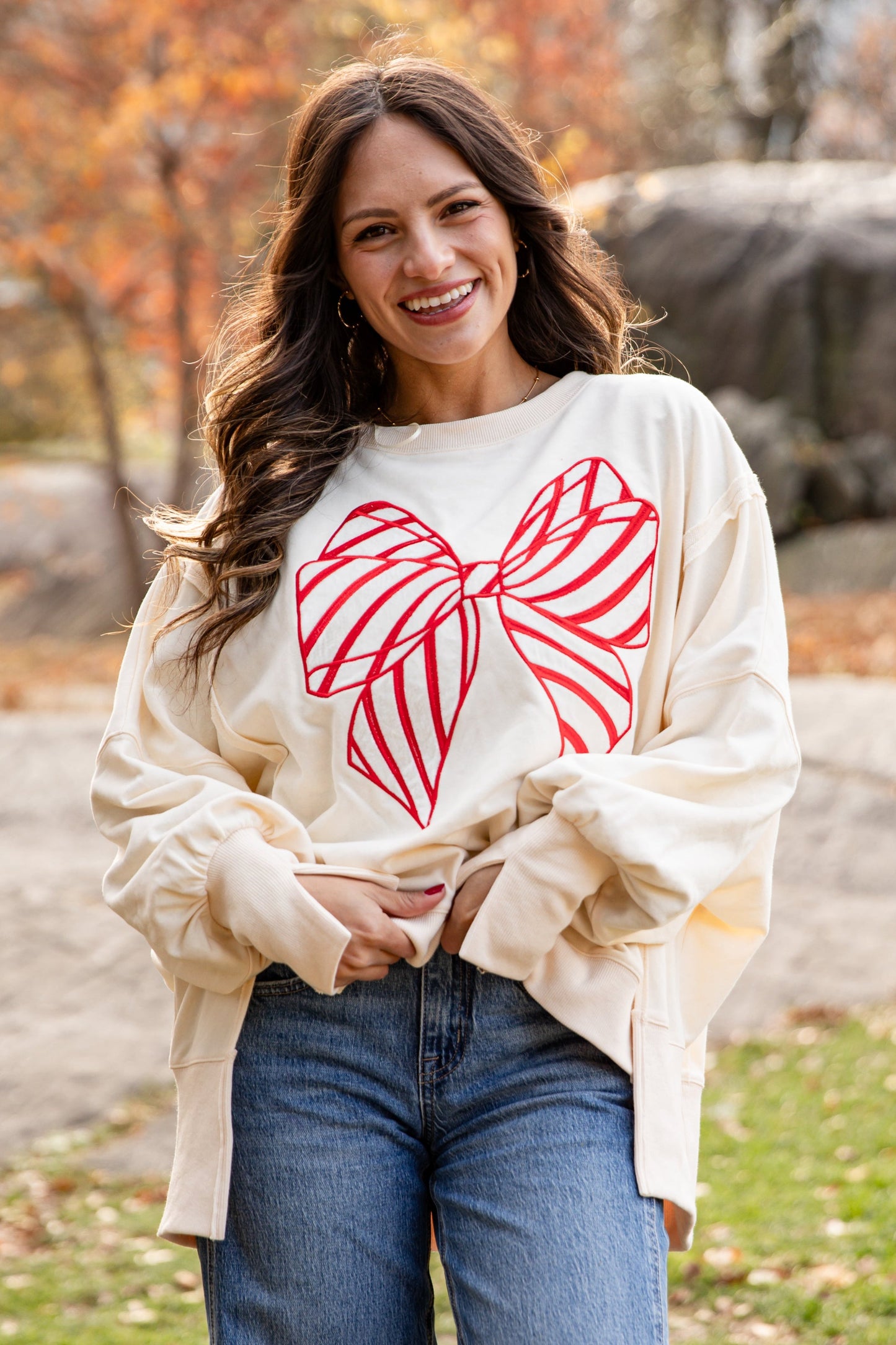 Woman wearing a cream sweatshirt with a red bow design outdoors in autumn.