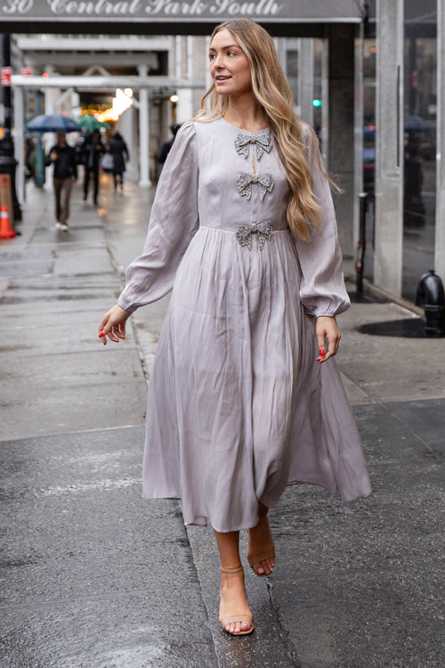 Woman in a light gray dress walking on a city street with '30 Central Park South' in the background.