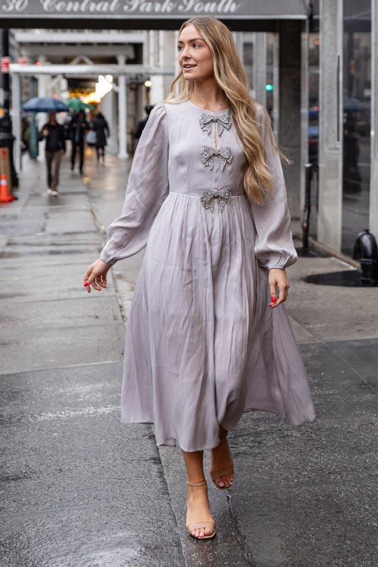 Woman in a light gray dress walking on a city street with '30 Central Park South' in the background.