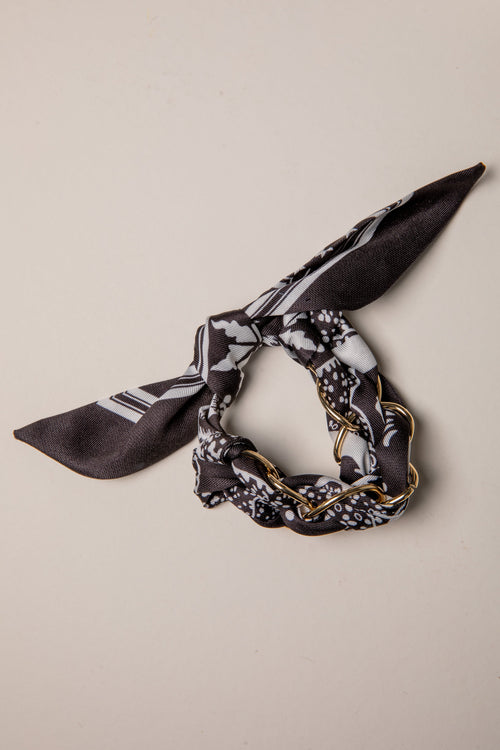Black and white patterned scarf with gold chain on a beige background