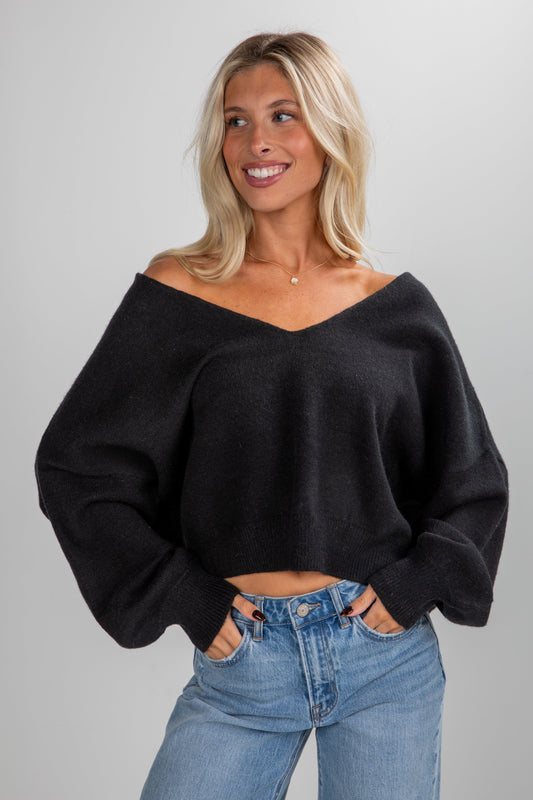 Woman wearing a black off-shoulder sweater and blue jeans on a gray background