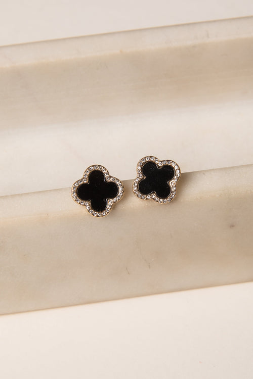 Black clover-shaped earrings on a beige surface
