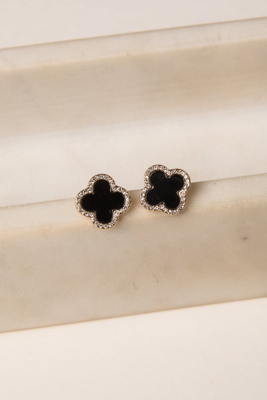Black clover-shaped earrings on a beige surface