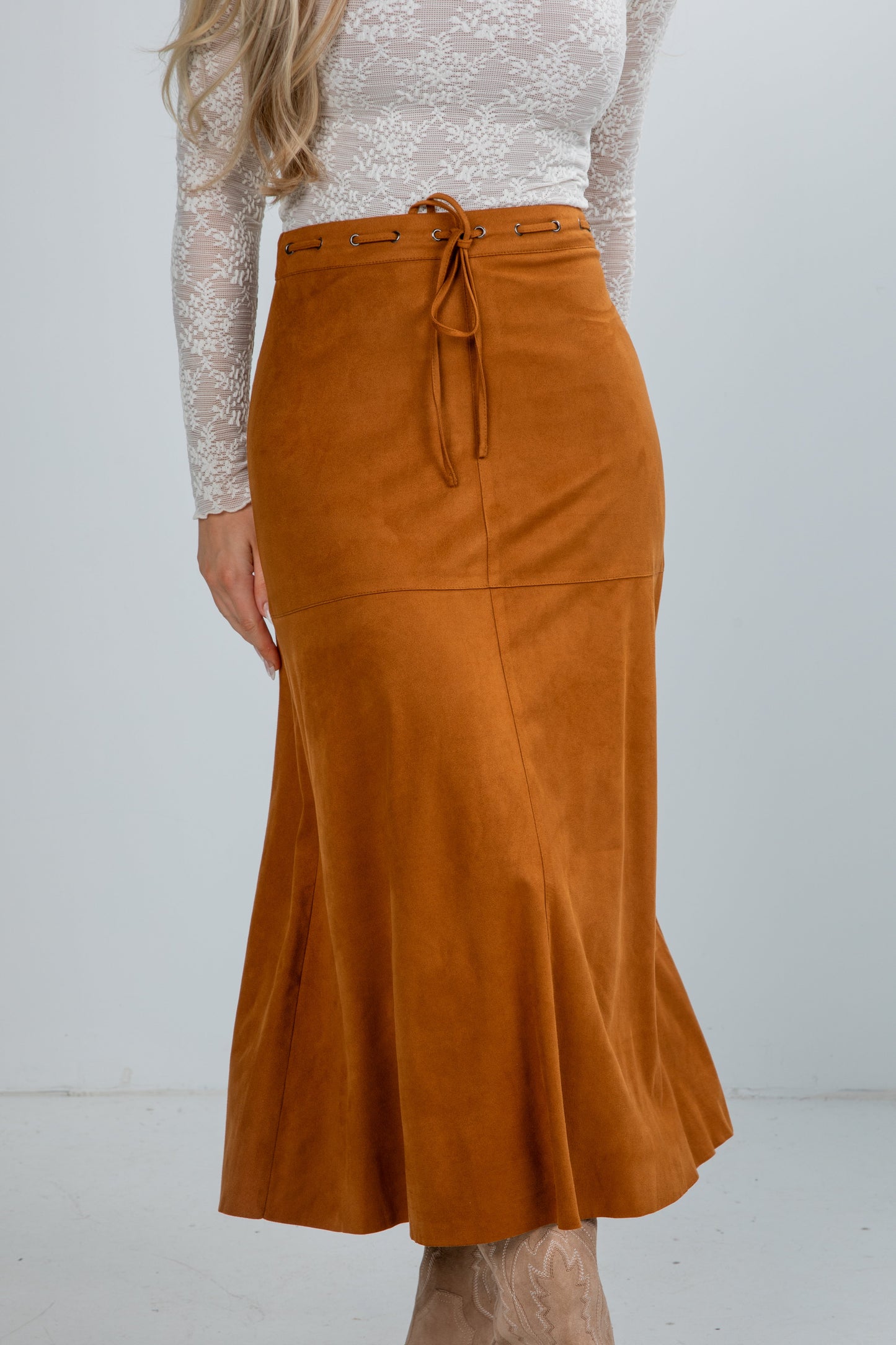 Person wearing a brown suede skirt with a white lace top on a plain background