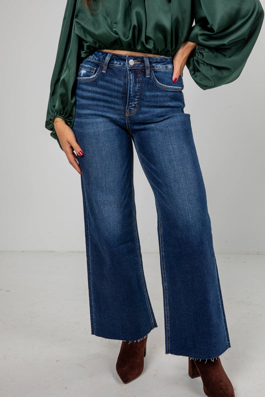 Person wearing blue flared jeans and a green top on a white background