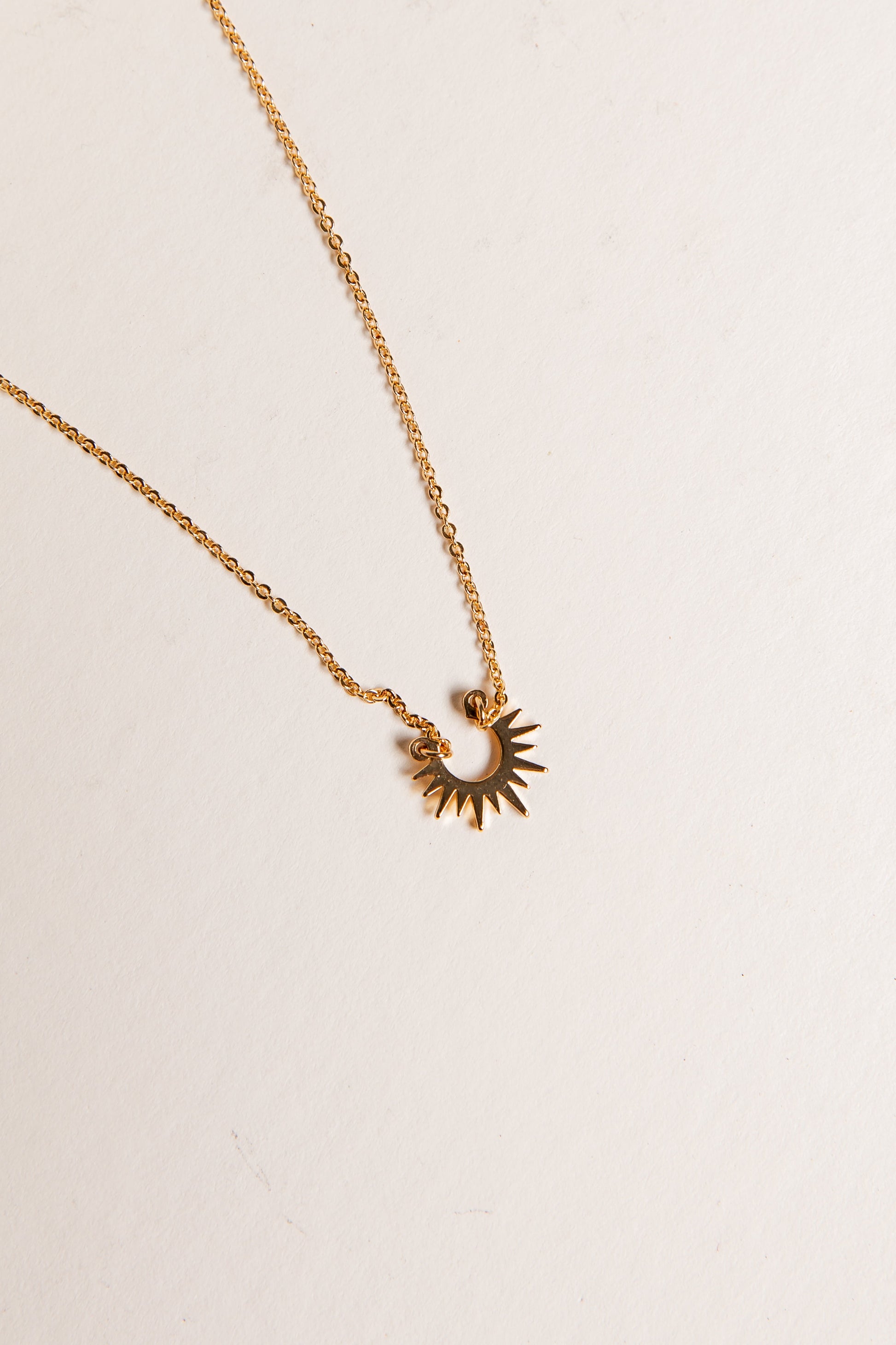 Gold necklace with a sun-shaped pendant on a light beige background