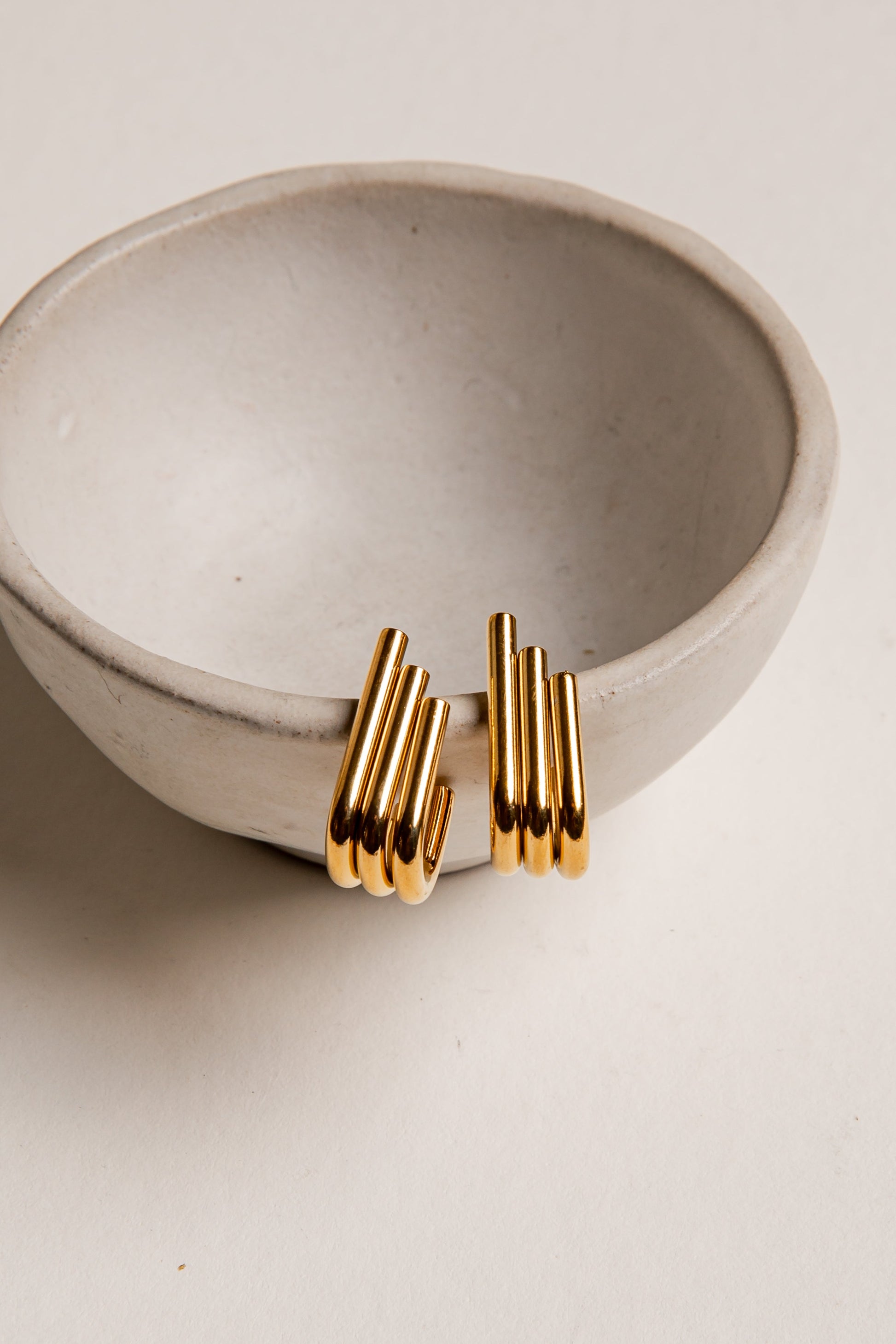 Gold earrings on a beige ceramic bowl