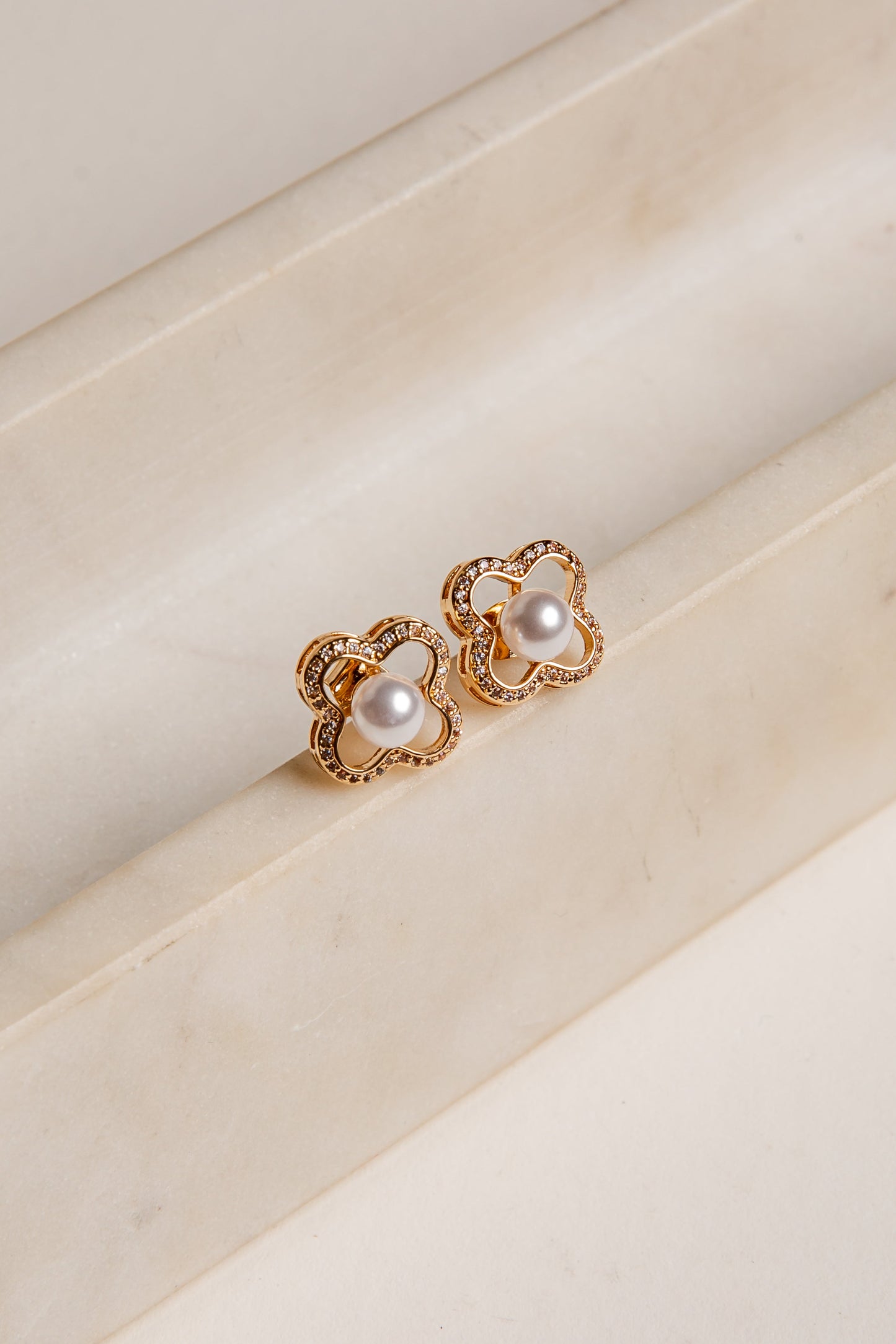 Gold earrings with pearl-like stones on a beige surface