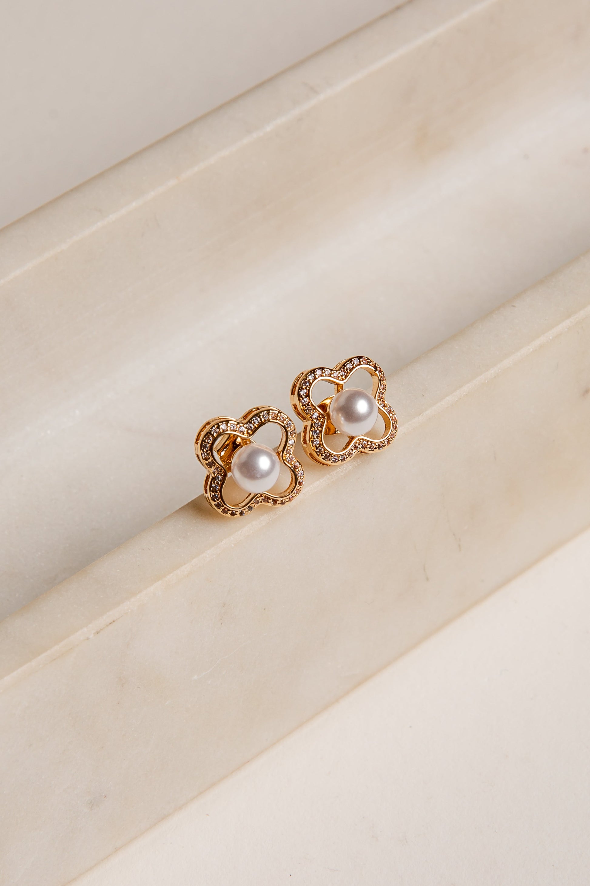 Gold earrings with pearl-like stones on a beige surface