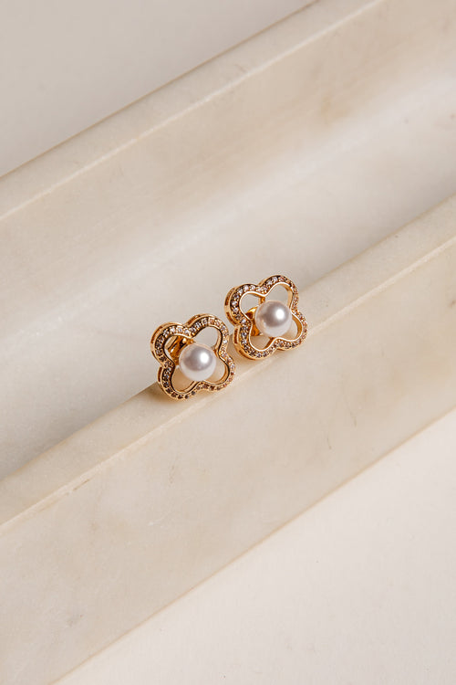 Gold earrings with pearl-like stones on a beige surface