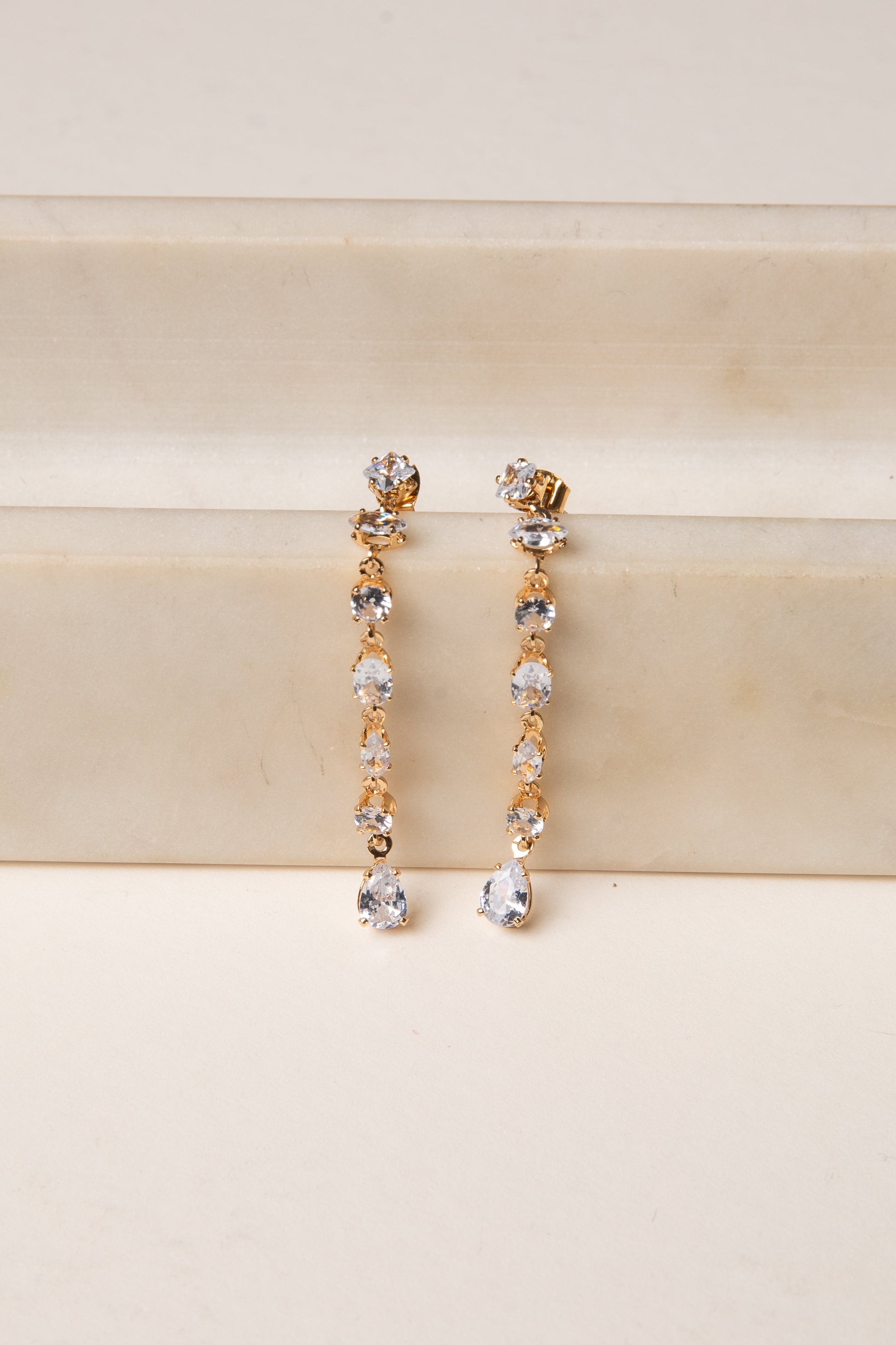 Gold and silver drop earrings on a beige surface