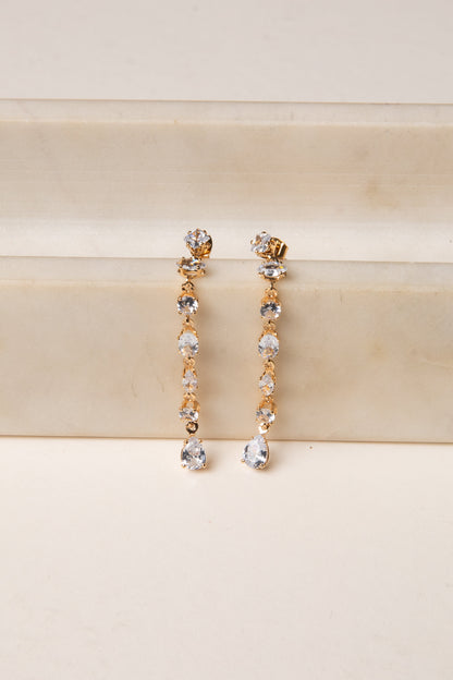Gold and silver drop earrings on a beige surface