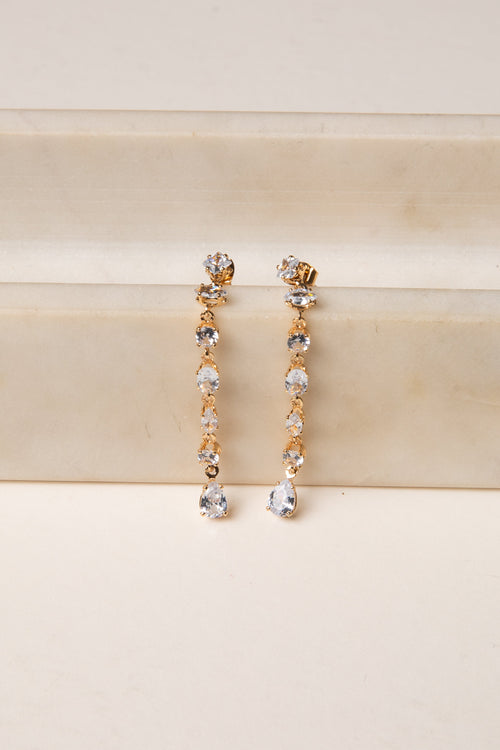 Gold and silver drop earrings on a beige surface