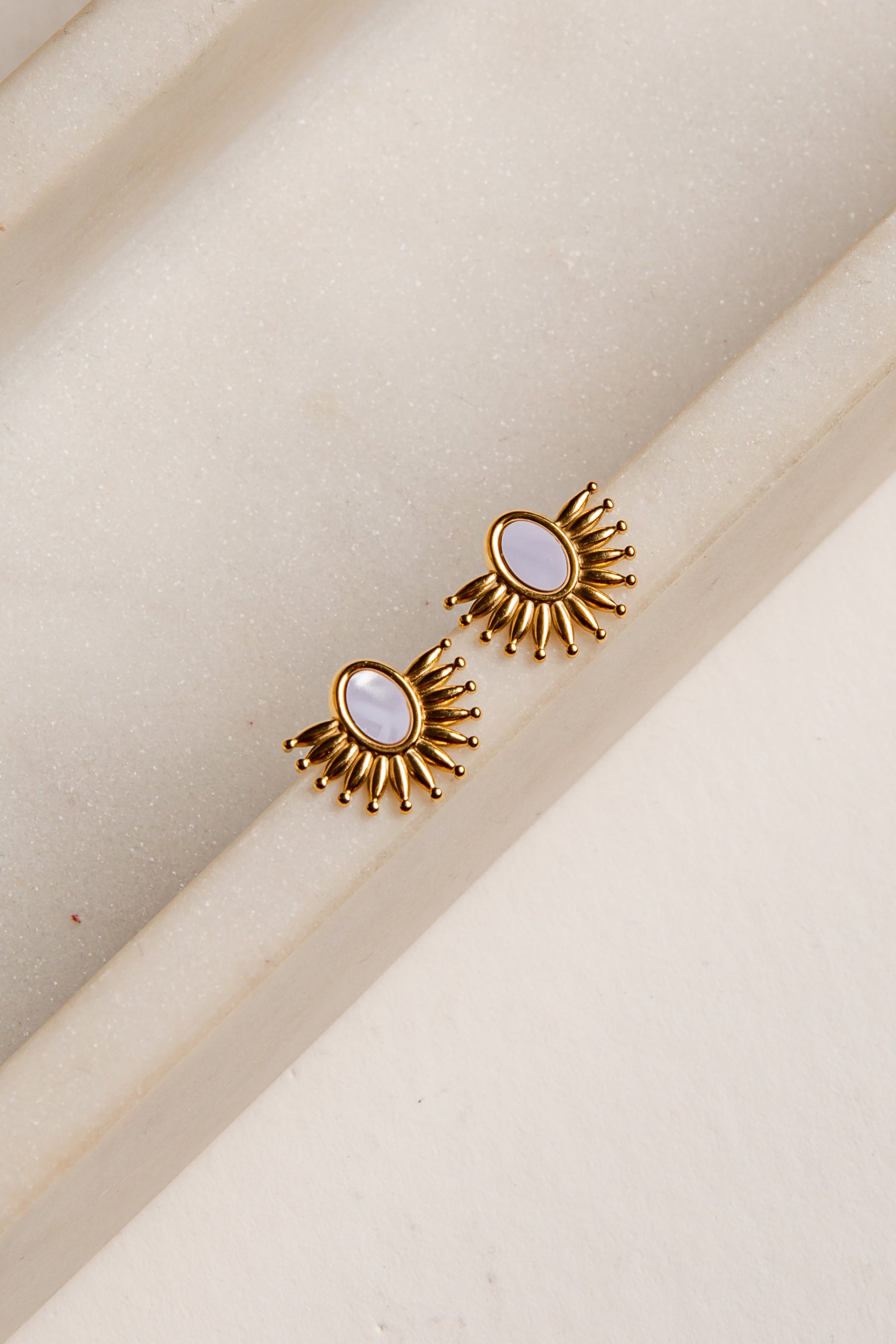 Gold earrings with a central gemstone on a beige background