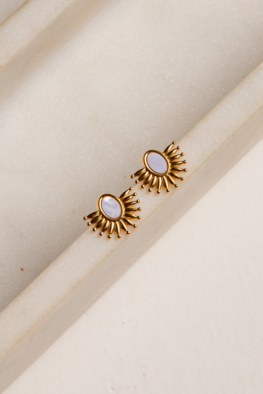 Gold earrings with a central gemstone on a beige background