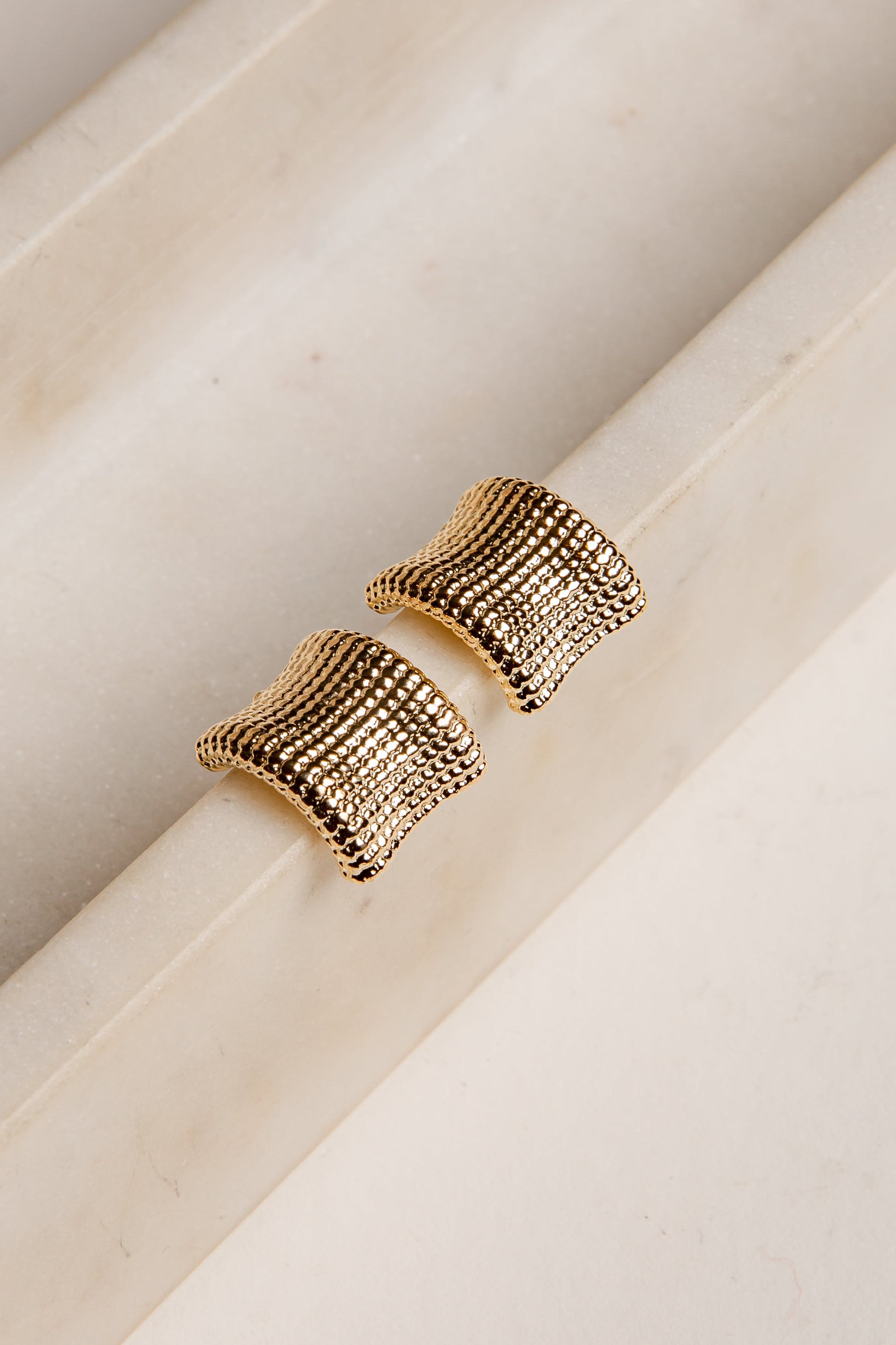 Gold textured earrings on a marble surface