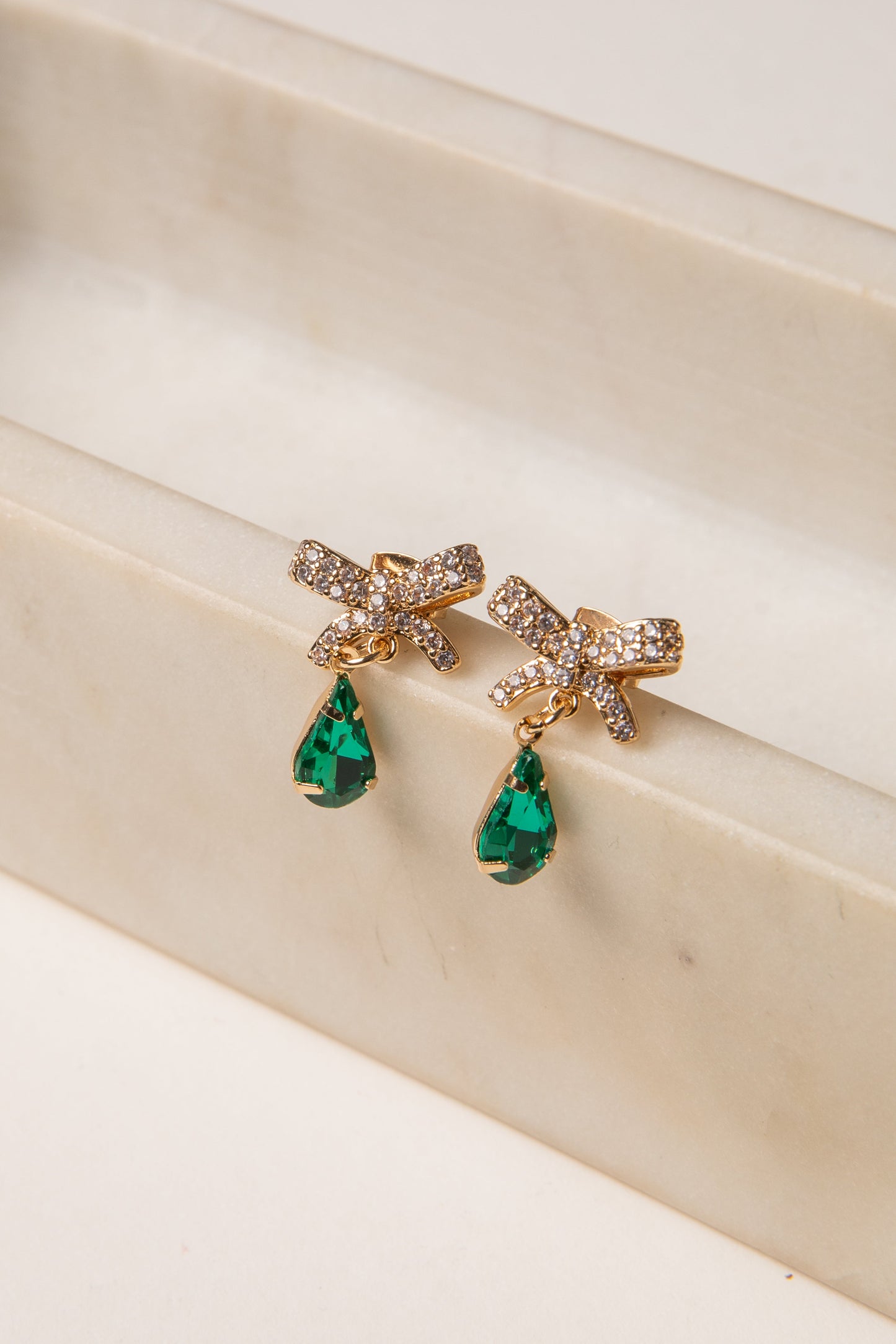 Gold earrings with green gemstones on a beige surface