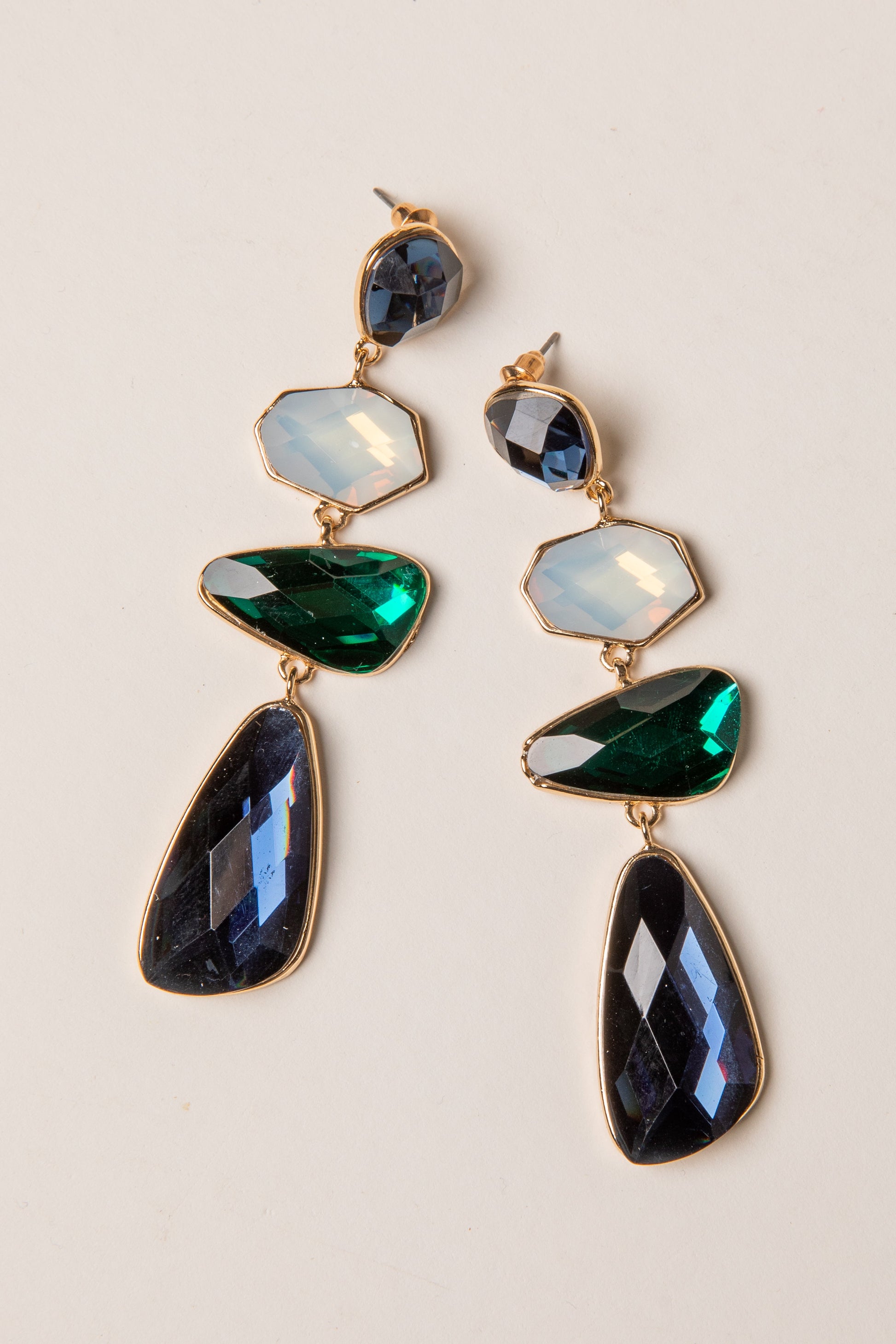 Pair of gold earrings with green and blue gemstones on a beige background