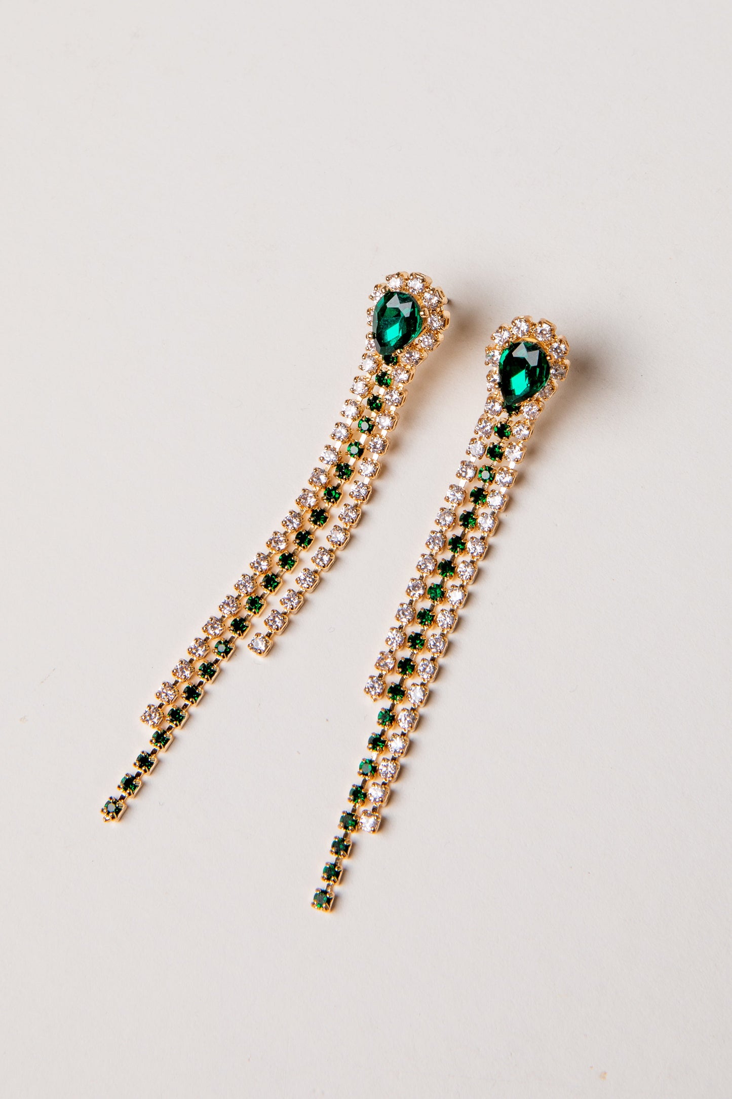 Pair of gold earrings with green gemstones on a light gray background