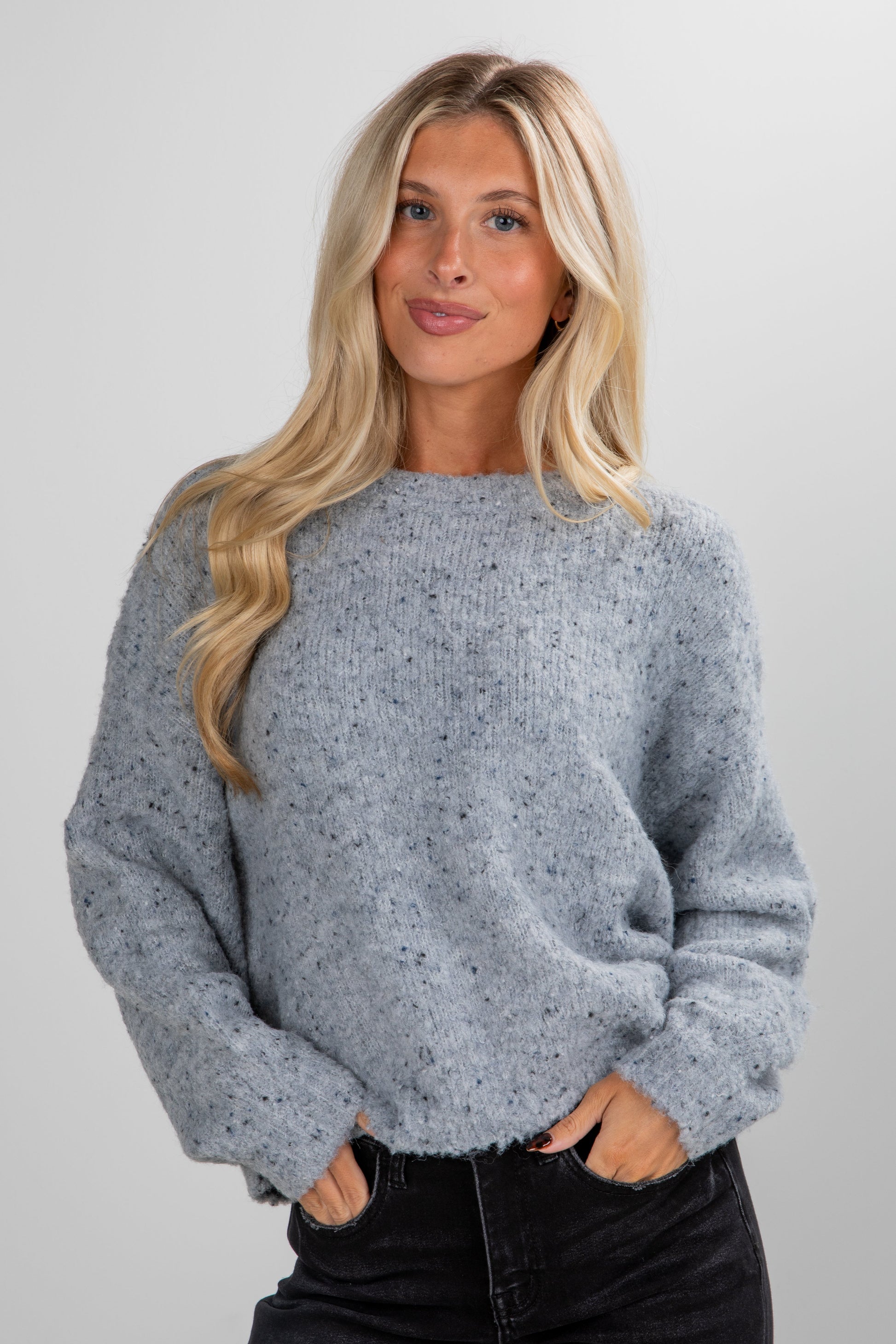Woman wearing a gray speckled sweater against a plain background