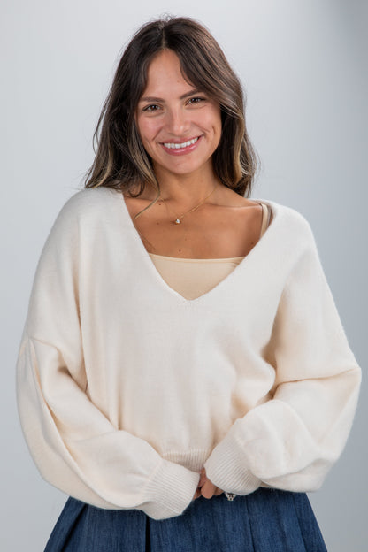 Woman wearing a cream sweater and blue skirt against a plain background