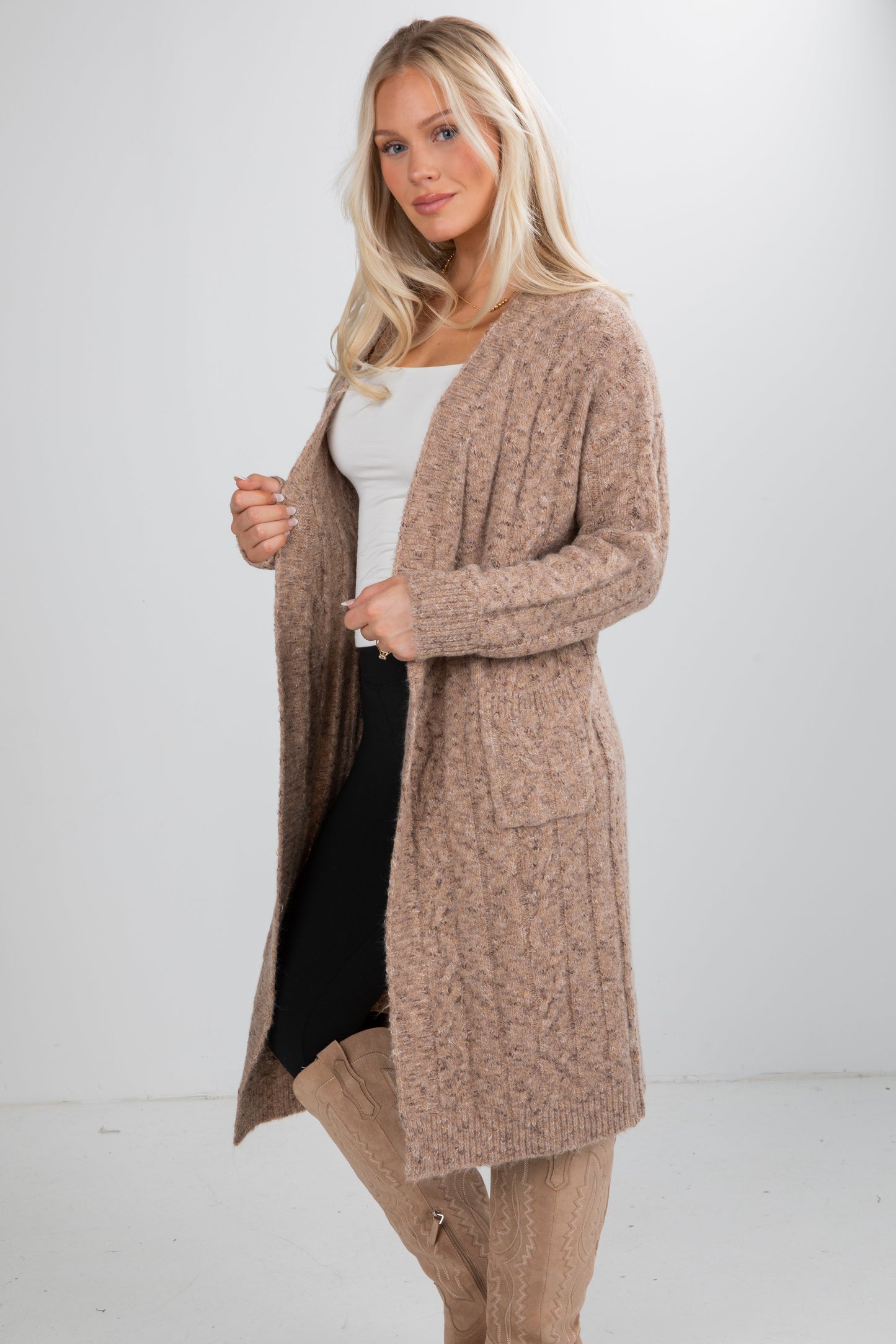 Woman wearing a long beige cardigan over a white top and black skirt on a white background