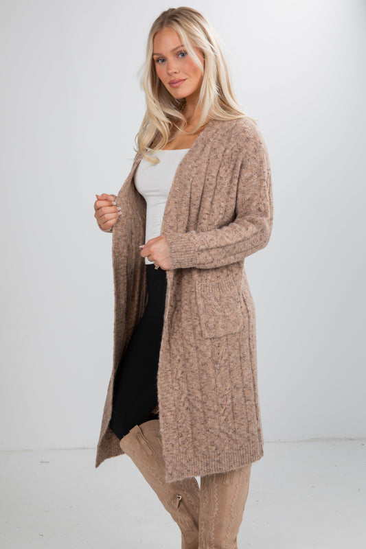 Woman wearing a long beige cardigan over a white top and black skirt on a white background