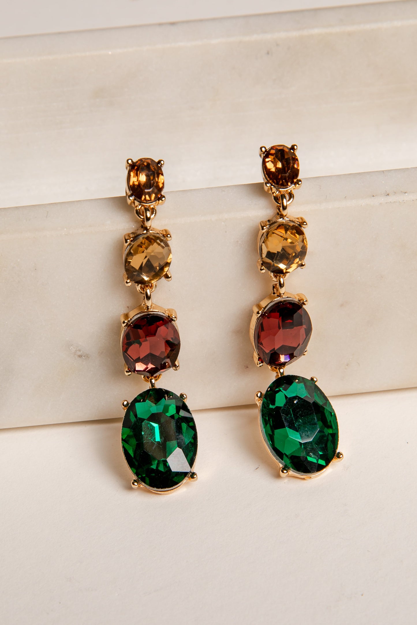 Pair of gold earrings with green and red gemstones on a light background