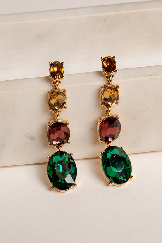 Pair of gold earrings with green and red gemstones on a light background