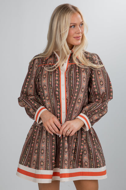 Woman wearing a patterned dress with orange accents on a gray background