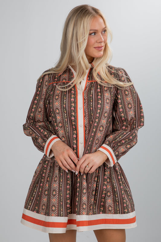 Woman wearing a patterned dress with orange accents on a gray background