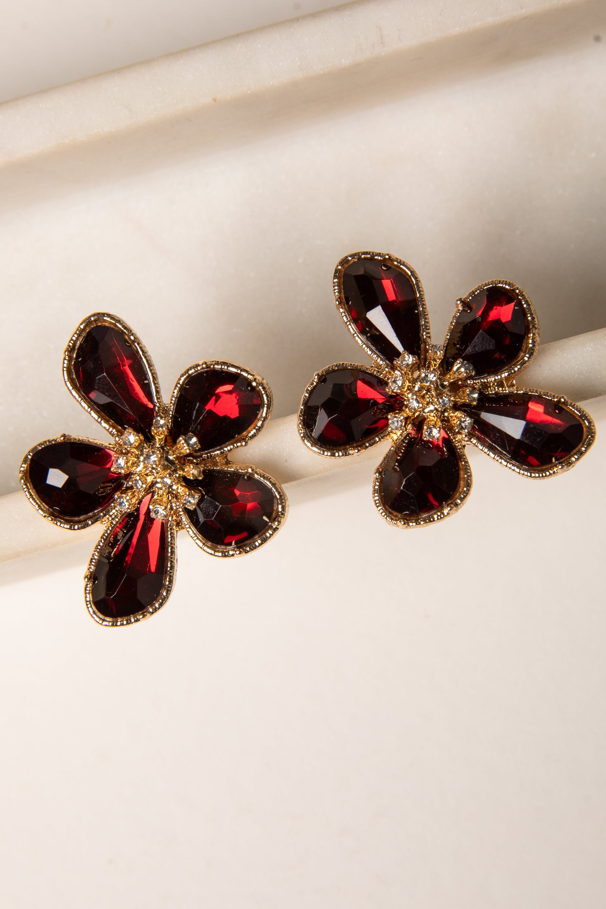 Flower-shaped earrings with red gemstones and gold accents on a light background