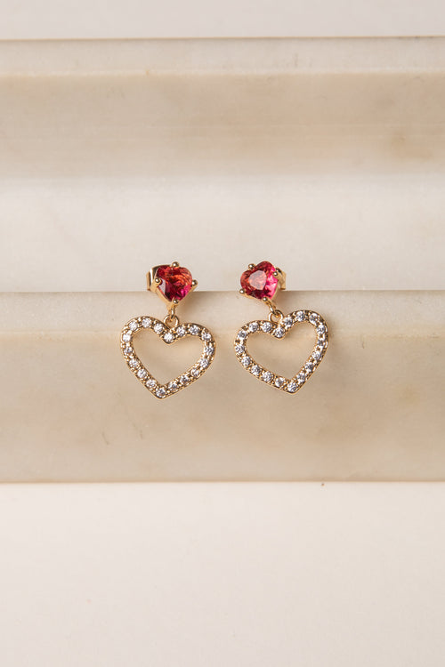 Heart-shaped earrings with red gemstones on a beige background