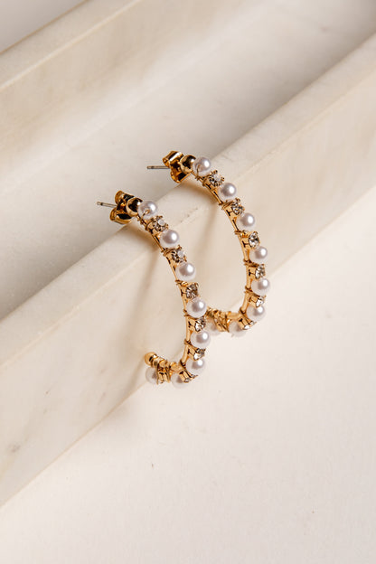 Gold hoop earrings with pearls on a beige surface