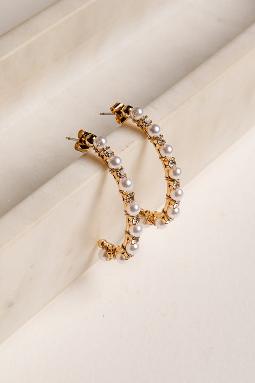Gold hoop earrings with pearls on a beige surface