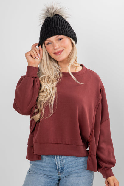 Woman wearing a maroon sweater, black beanie with pom-pom, and blue jeans on a white background